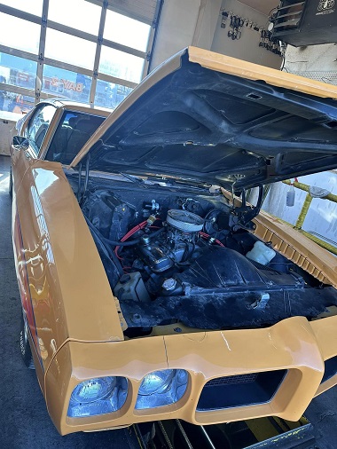 Yellow 1970s Pontiac GTO in service bay with hood up at Wasilla Lube Express