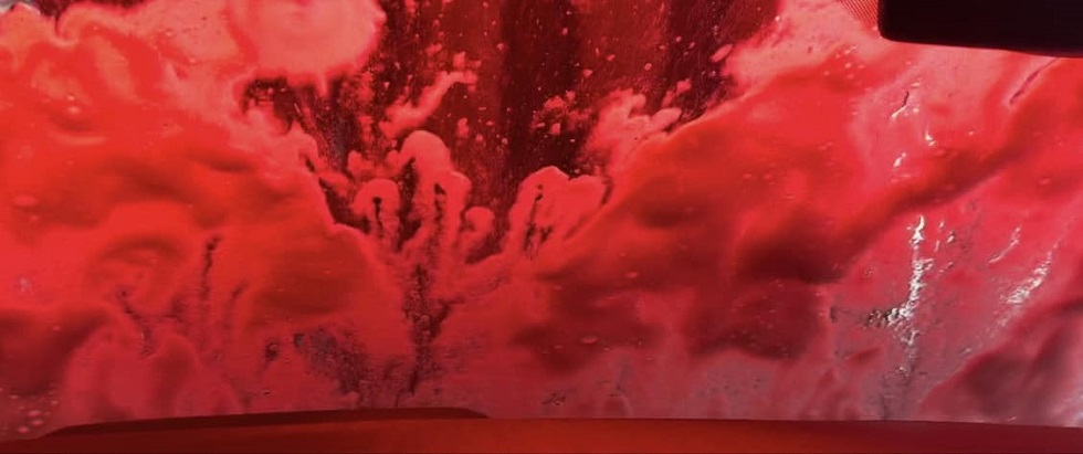 Soap and water on windshield as car goes through hot tunnel car wash in Wasilla, AK; the background lights in the car wash tunnel are a vibrant red